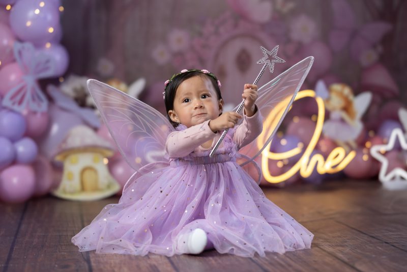 Niña pequeña vestida de hada levantando una varita mágica plateada durante su sesión de fotos de cumpleaños número uno