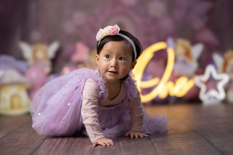 Bebé gateando con vestido de tul lila en sesión de fotos de primer año con temática de hadas y fondo desenfocado