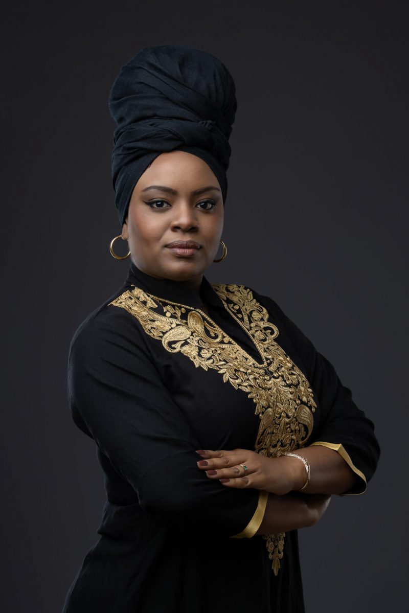 Mujer con vestimenta formal negra y bordados dorados con turbante, pose de confianza para perfil ejecutivo.