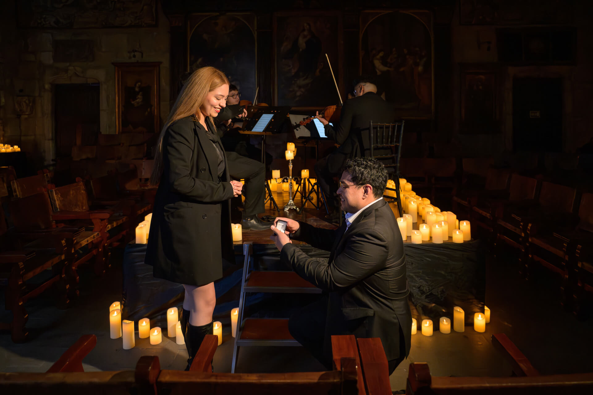 Fotografía de compromiso: novio de rodillas pidiendo matrimonio en la Capilla Gótica con músicos de fondo, Teran Studios