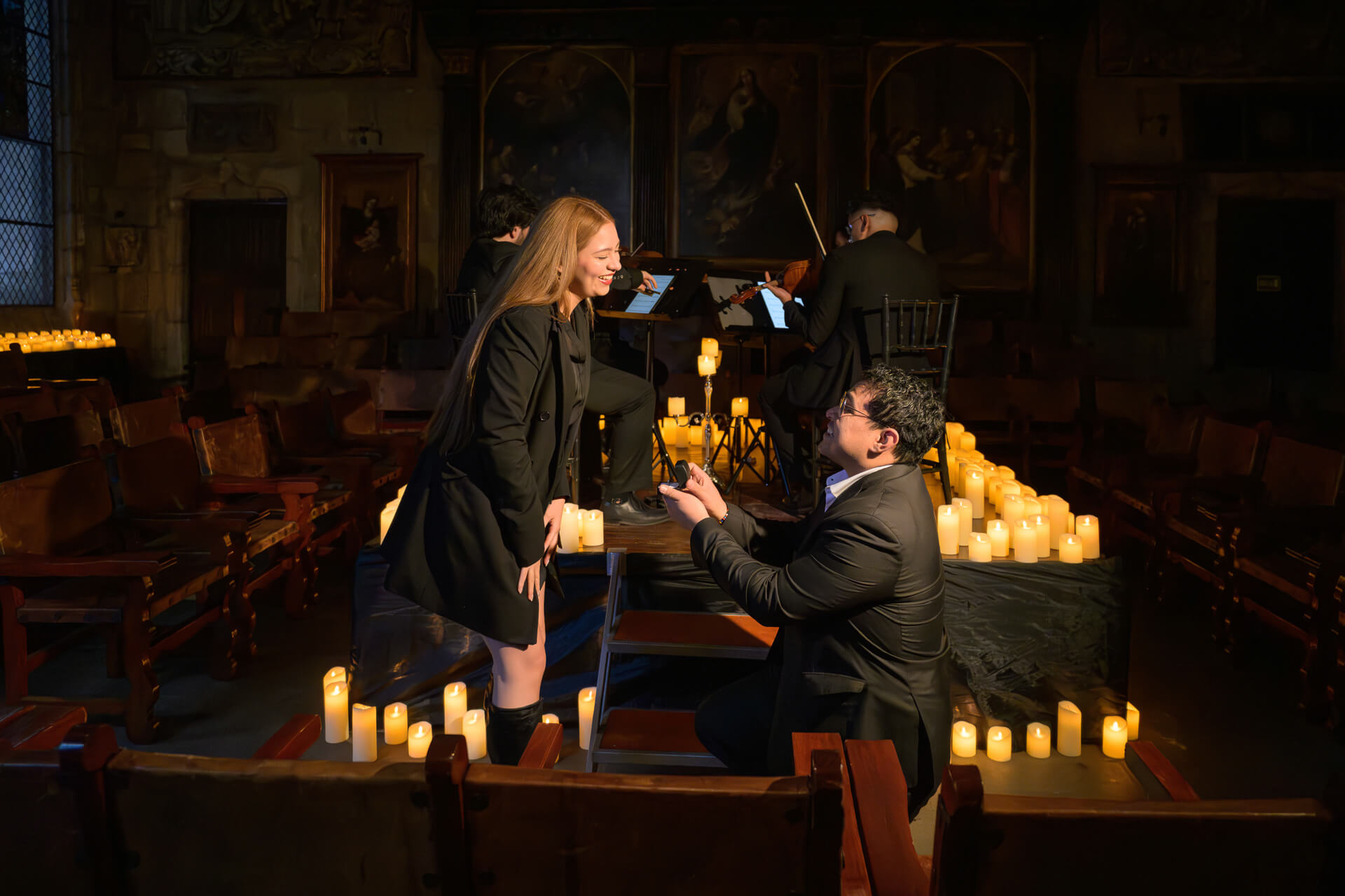 Fotografía de compromiso: novio de rodillas pidiendo matrimonio en la Capilla Gótica con músicos de fondo, Teran Studios